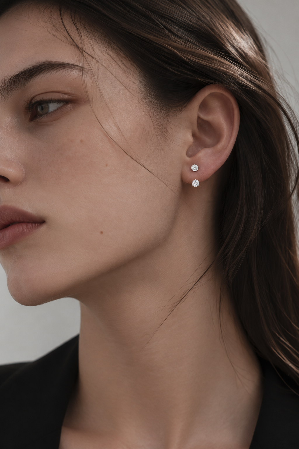 HERIMYST double diamond stud earrings with a smaller upper diamond and larger lower diamond worn on the earlobe.