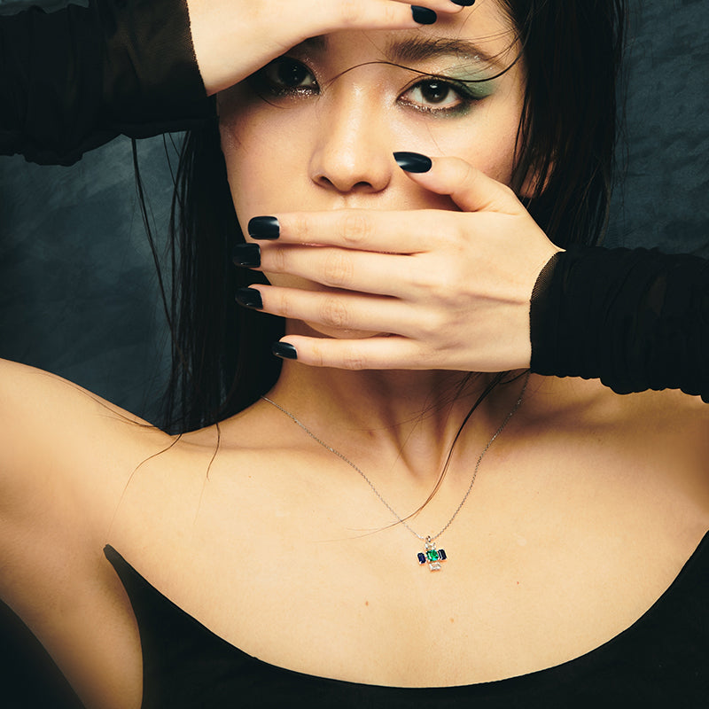 Model wearing an architectural cross gemstone pendant necklace in 14K white gold with lab-grown diamond, emerald, and sapphire, styled with a minimalist black