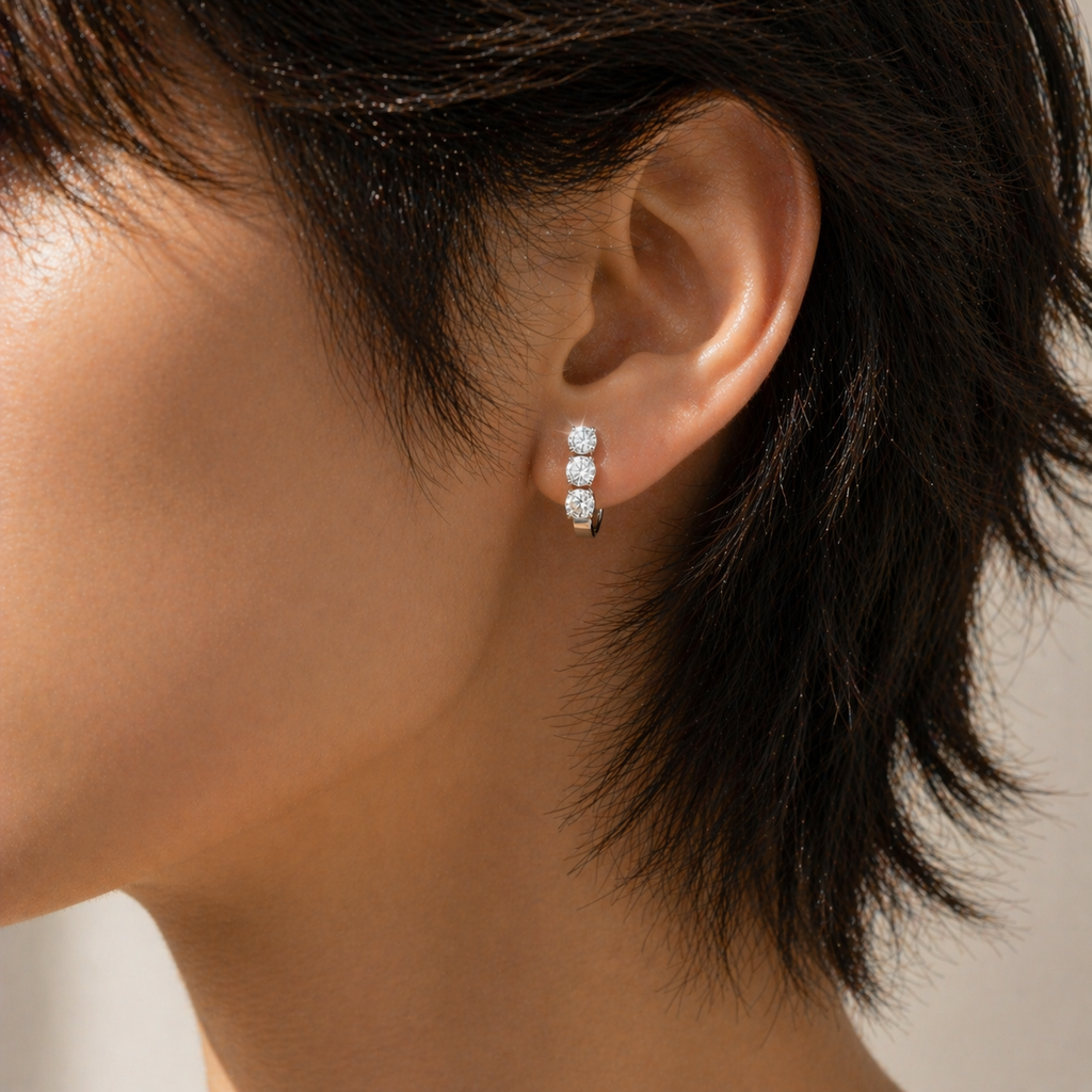 Three stone diamond huggie earrings on ear, round cut lab grown diamonds, unisex minimalist stud earring close-up with natural fire