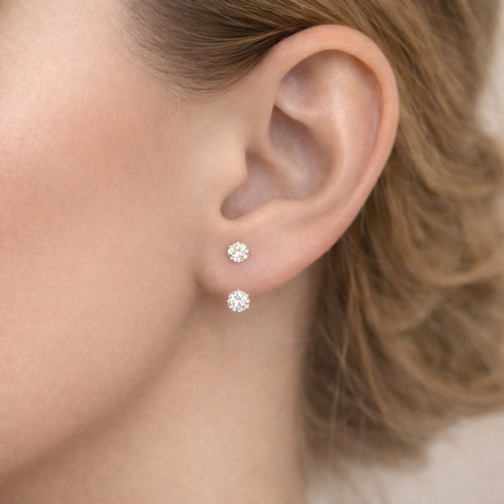Close-up side view of a woman’s ear wearing two minimalist lab-grown diamond stud earrings, featuring round brilliant-cut diamonds with subtle sparkle in a clean, elegant fine jewelry style.