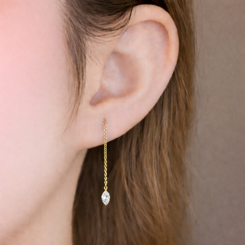 Close-up of a 14K gold threader earring with a small marquise-cut diamond, showing refined facets and natural light reflection on the diamond surface.