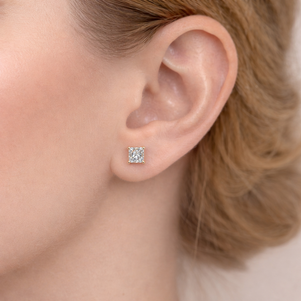 Close-up side view of a woman’s ear wearing a refined princess-cut lab-grown diamond stud earring, set in yellow gold with four prongs, featuring enhanced brilliance and natural sparkle in an elegant fine jewelry style.