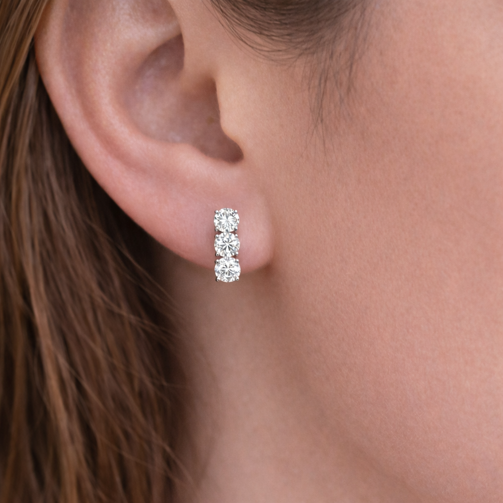 Three-stone lab-grown diamond huggie earrings worn on ear, 14K white gold, subtle everyday sparkle