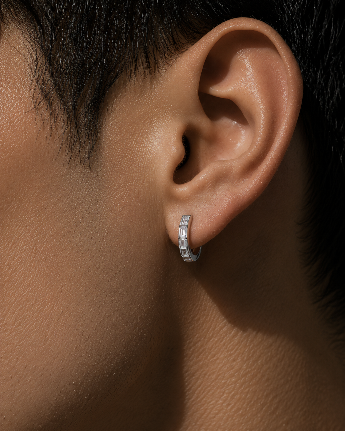 Close-up detail of a male model wearing a 12mm invisible set baguette diamond hoop earring in 14K white gold by HERIMYST
