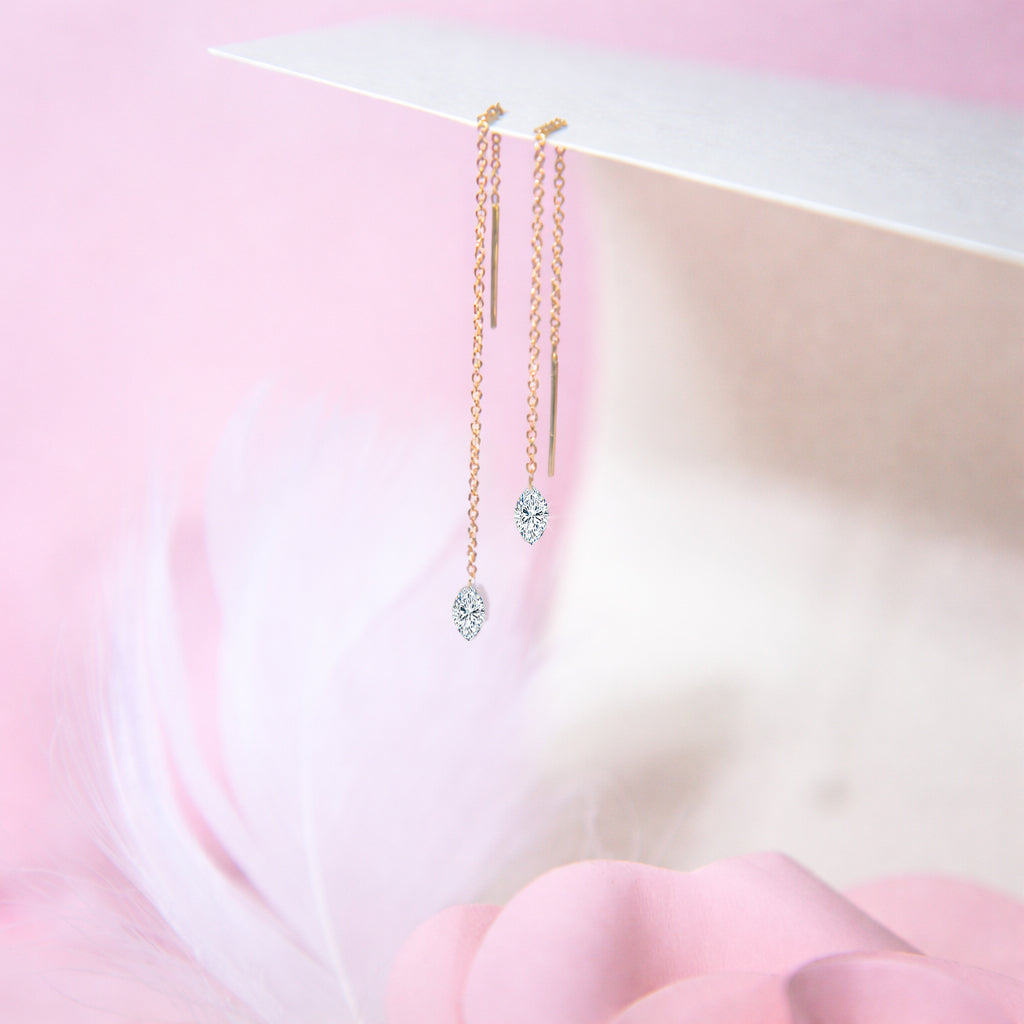 Pair of floating diamond threader earrings in 14K yellow gold with lab-grown marquise-cut diamonds against a soft pink floral background