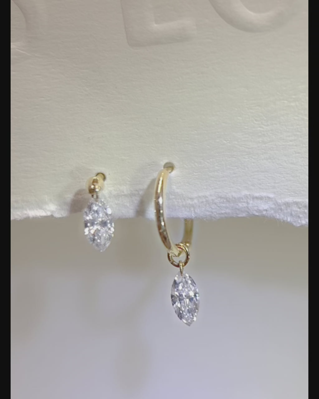 Marquise floating diamond drop huggie earrings, showing the suspended diamond swinging freely as reflections shift across its facets.