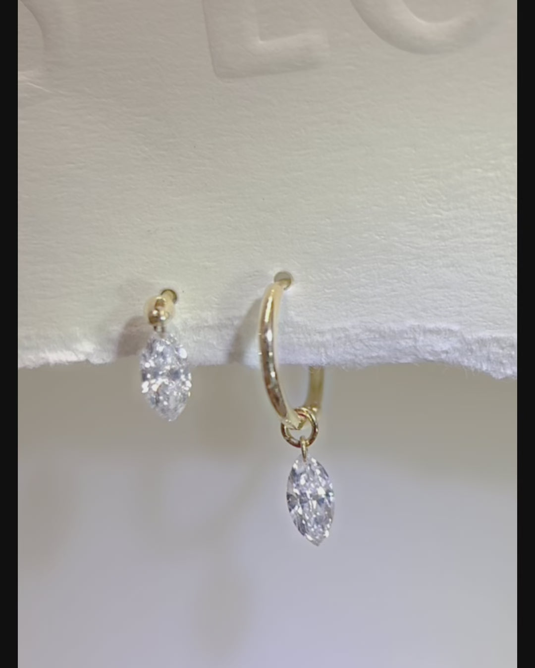Marquise floating diamond drop huggie earrings, showing the suspended diamond swinging freely as reflections shift across its facets.